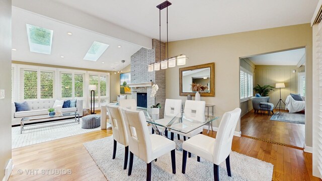 dining room featuring plenty of natural light, wood finished floors, lofted ceiling with skylight, and a fireplace