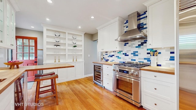 kitchen with beverage cooler, wall chimney exhaust hood, high end stainless steel range oven, and wooden counters