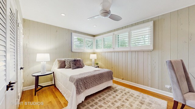 bedroom featuring baseboards, ceiling fan, wood walls, and wood finished floors