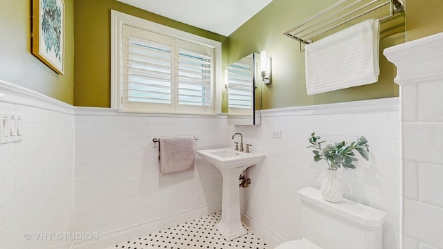 bathroom with toilet, tile walls, and a wainscoted wall