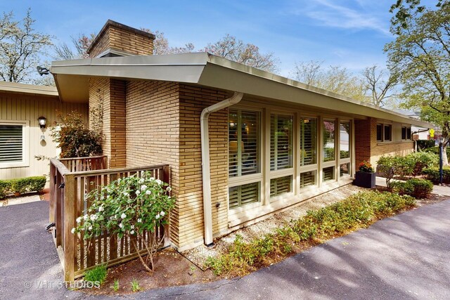 view of side of home featuring brick siding, a chimney, and a deck