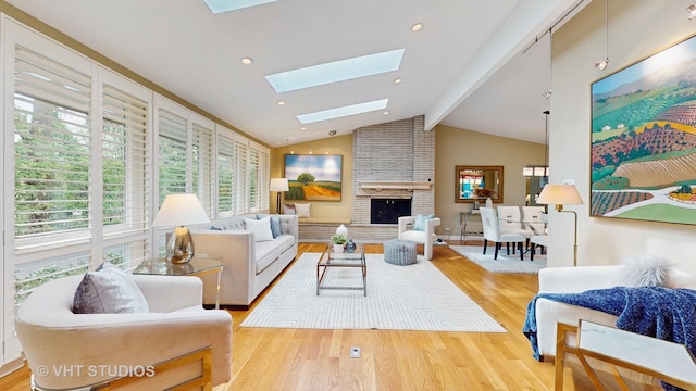 living room with vaulted ceiling with skylight, a brick fireplace, and wood finished floors