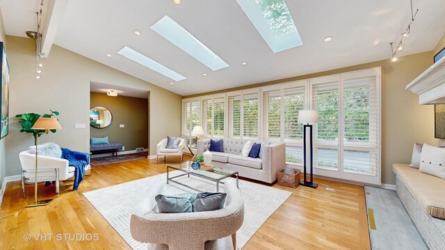 living room with vaulted ceiling with skylight, baseboards, light wood finished floors, and rail lighting