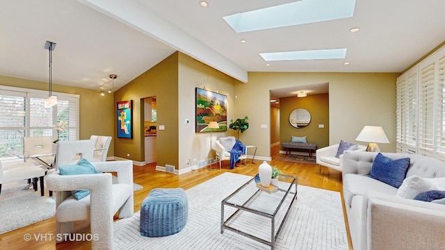 living room featuring baseboards, light wood finished floors, and lofted ceiling with skylight