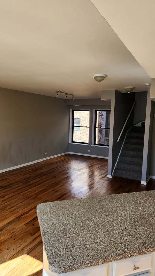 unfurnished living room featuring baseboards, wood finished floors, rail lighting, and stairs