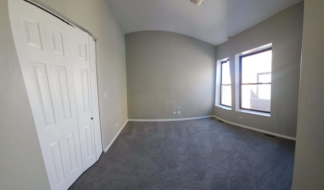 empty room featuring baseboards, lofted ceiling, and dark colored carpet