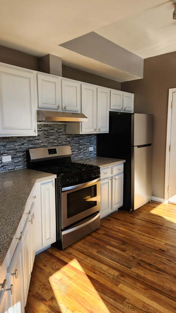 kitchen with white cabinets, dark wood-style flooring, backsplash, under cabinet range hood, and appliances with stainless steel finishes