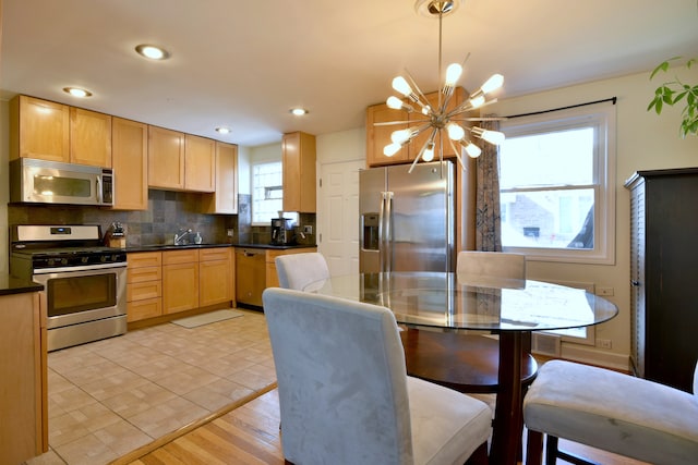kitchen with a notable chandelier, light brown cabinets, dark countertops, decorative backsplash, and appliances with stainless steel finishes
