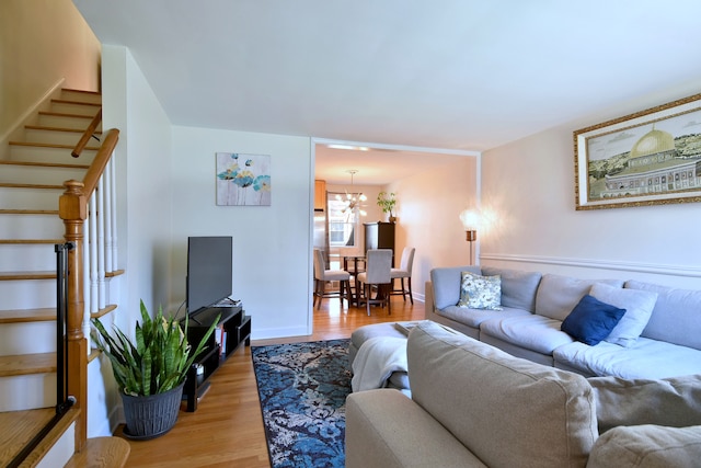 living room with a chandelier, light wood finished floors, baseboards, and stairway