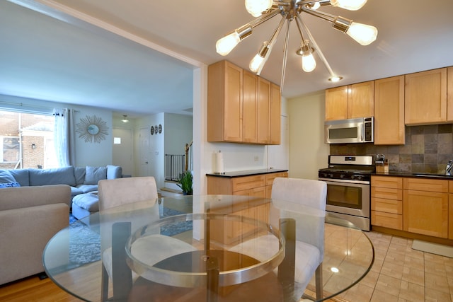 kitchen with appliances with stainless steel finishes, dark countertops, open floor plan, a notable chandelier, and backsplash