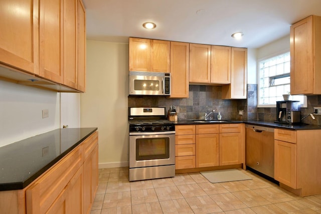 kitchen featuring tasteful backsplash, light brown cabinets, dark countertops, stainless steel appliances, and a sink