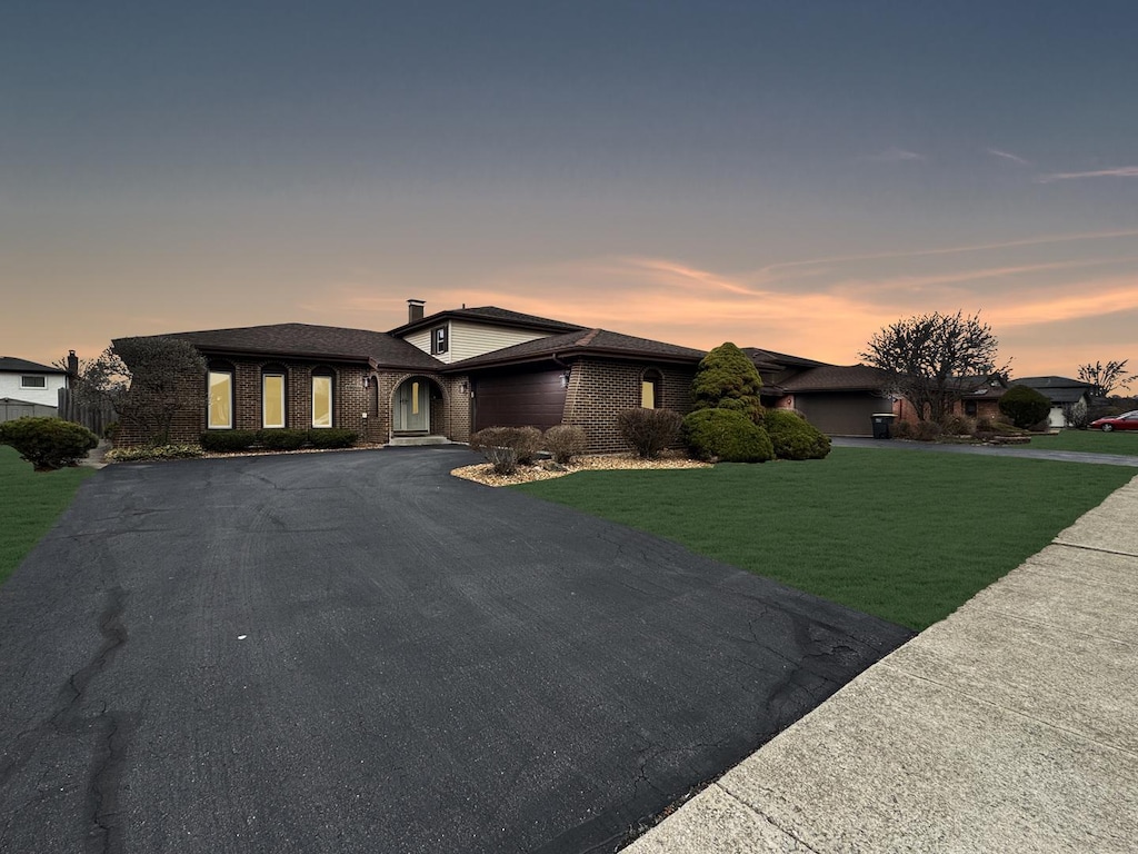 view of front facade featuring brick siding, a front yard, aphalt driveway, and a garage