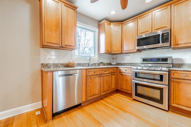 kitchen featuring baseboards, light wood-type flooring, light stone counters, appliances with stainless steel finishes, and backsplash