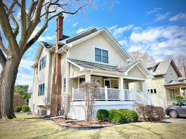 view of front of property featuring a porch, cooling unit, a chimney, and a front yard