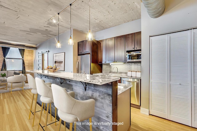 110 N Peoria St Unit 205, Chicago, IL 60607 - kitchen with stainless steel appliances, light wood finished floors, decorative backsplash, a kitchen breakfast bar, and decorative light fixtures