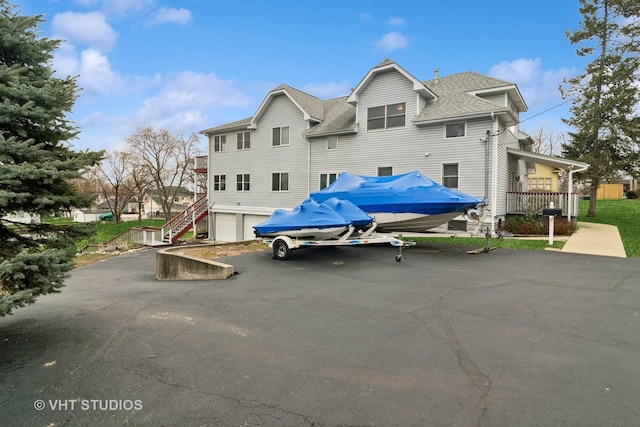 exterior space featuring a garage, aphalt driveway, stairway, and a shingled roof