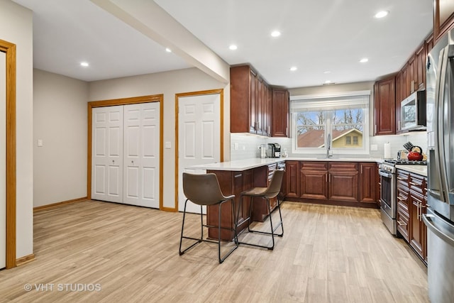 kitchen featuring a sink, a kitchen bar, light wood finished floors, stainless steel appliances, and backsplash
