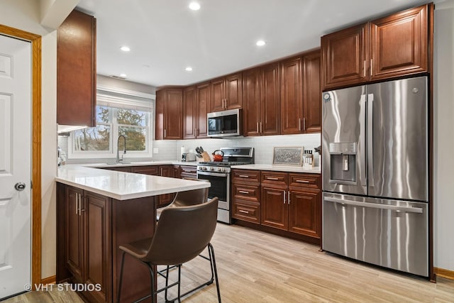 kitchen featuring a peninsula, light countertops, decorative backsplash, stainless steel appliances, and a sink