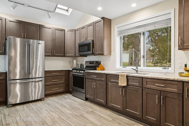 kitchen featuring light wood-style flooring, appliances with stainless steel finishes, decorative backsplash, and a sink