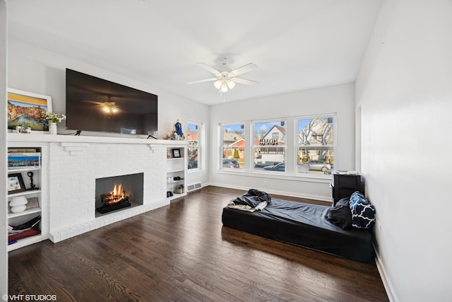 sitting room with wood finished floors, visible vents, a ceiling fan, and a brick fireplace
