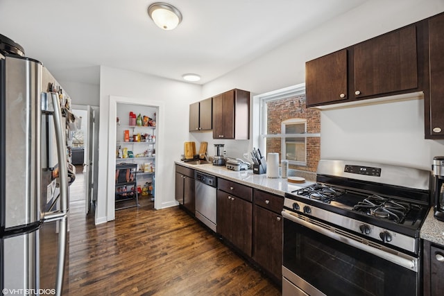 kitchen with dark brown cabinetry, dark wood-type flooring, appliances with stainless steel finishes, light stone counters, and a sink