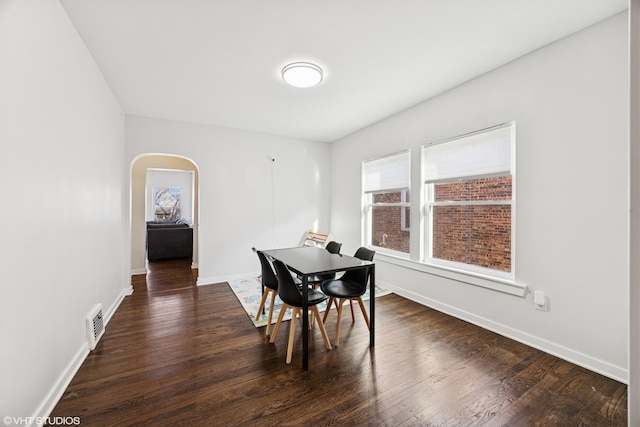 dining room featuring visible vents, baseboards, arched walkways, and dark wood finished floors