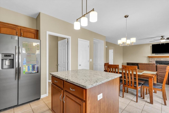 kitchen with a kitchen island, stainless steel refrigerator with ice dispenser, pendant lighting, ceiling fan with notable chandelier, and light tile patterned flooring