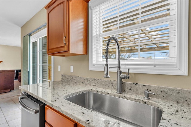 kitchen with light stone countertops, a sink, dishwasher, brown cabinetry, and light tile patterned floors