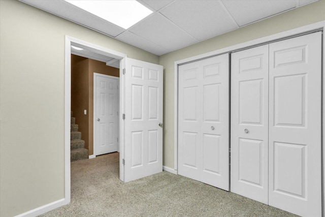 unfurnished bedroom featuring carpet floors, baseboards, a paneled ceiling, and a closet