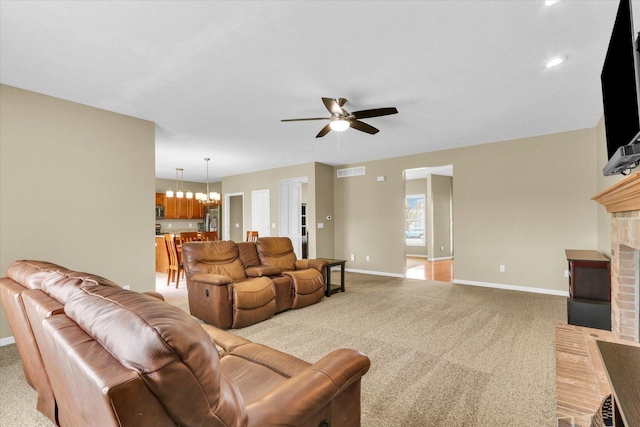 living room with light colored carpet, a brick fireplace, ceiling fan with notable chandelier, baseboards, and visible vents