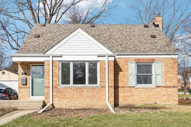 view of front of property with roof with shingles, a chimney, an outbuilding, brick siding, and a garage