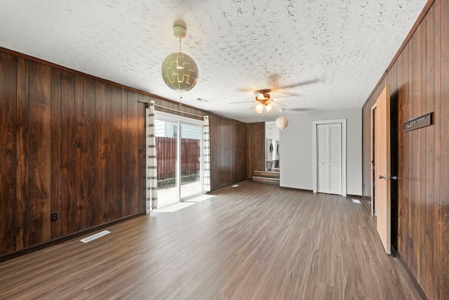 120 Anderson Ave, Joliet, IL 60433 - unfurnished living room featuring wood walls, wood finished floors, ceiling fan, baseboards, and a textured ceiling