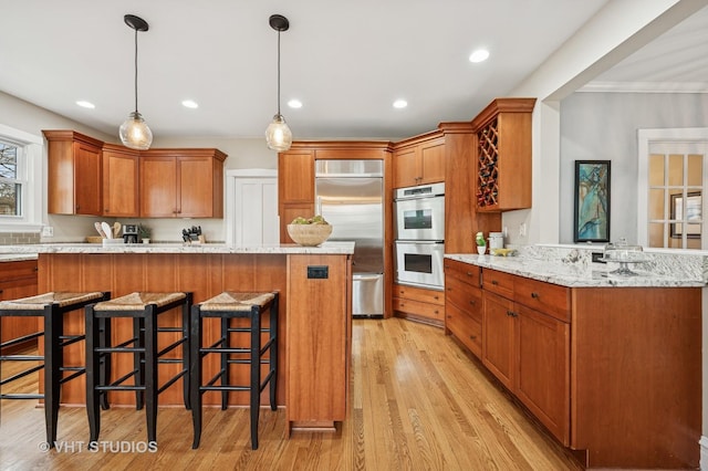 kitchen with light stone counters, a kitchen breakfast bar, stainless steel appliances, light wood finished floors, and a peninsula