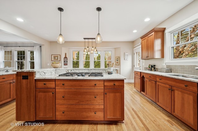 kitchen featuring stainless steel gas stovetop, a sink, light wood-style floors, and a healthy amount of sunlight