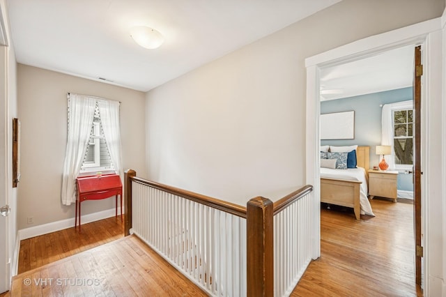 hall with hardwood / wood-style flooring, baseboards, and an upstairs landing
