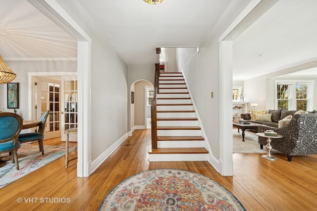 stairway with arched walkways, baseboards, and hardwood / wood-style flooring