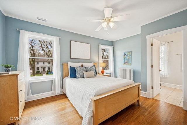 bedroom featuring radiator heating unit, wood finished floors, multiple windows, and visible vents