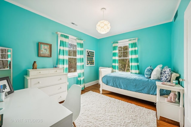 bedroom featuring baseboards, ornamental molding, wood finished floors, and visible vents