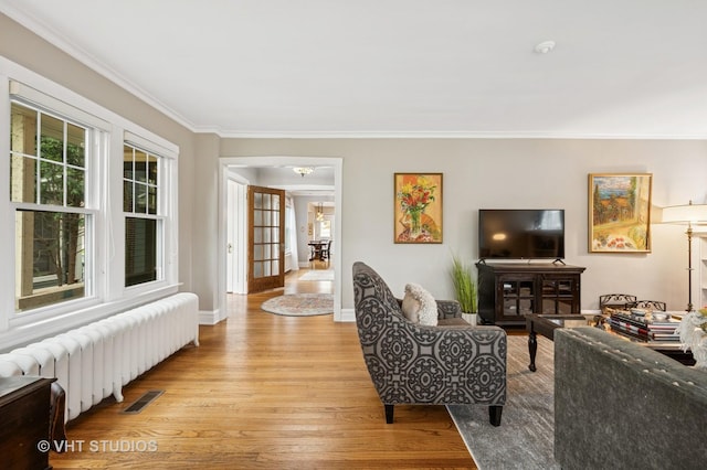 living area with baseboards, visible vents, radiator heating unit, wood finished floors, and ornamental molding