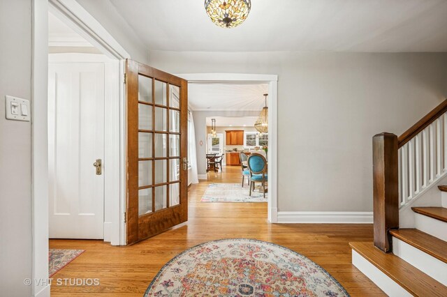 entryway with baseboards, wood finished floors, stairs, and a notable chandelier