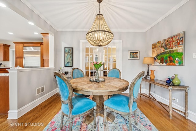 dining space featuring light wood finished floors, baseboards, visible vents, a notable chandelier, and ornamental molding