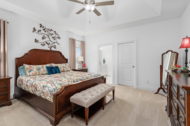 bedroom with a tray ceiling, baseboards, light carpet, and connected bathroom