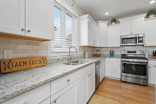 kitchen with decorative backsplash, light wood-style flooring, appliances with stainless steel finishes, white cabinetry, and a sink