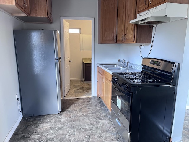 kitchen featuring light countertops, a sink, freestanding refrigerator, under cabinet range hood, and range with gas cooktop
