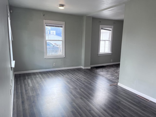empty room with dark wood-style floors, baseboards, and visible vents