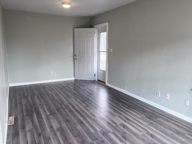 spare room featuring dark wood-type flooring, visible vents, and baseboards