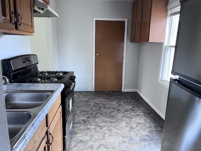 kitchen featuring light countertops, freestanding refrigerator, under cabinet range hood, baseboards, and black range with gas cooktop
