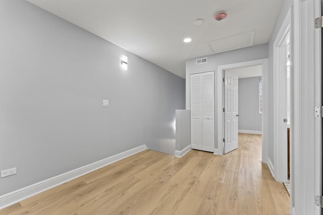 empty room with light wood-style flooring, baseboards, attic access, and visible vents
