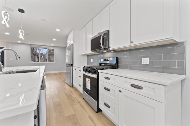kitchen with white cabinetry, backsplash, a sink, light wood-style flooring, and appliances with stainless steel finishes