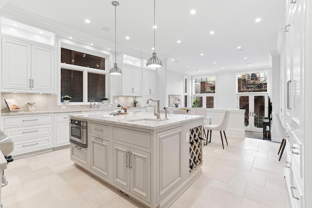 kitchen featuring white cabinetry, a center island with sink, a sink, and crown molding